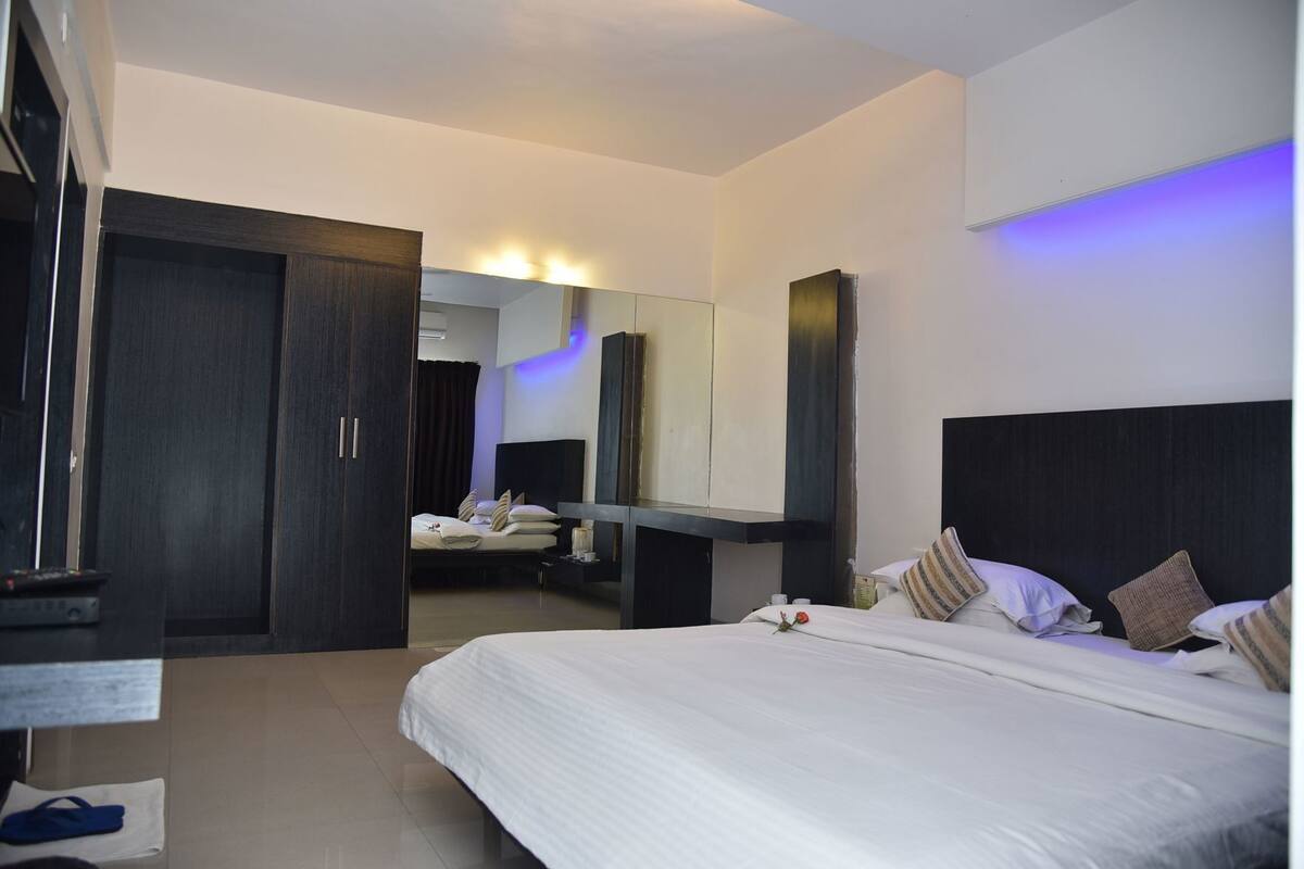 A modern hotel room with a large bed, a wardrobe, a vanity with a mirror, and a bathroom visible through an open door.