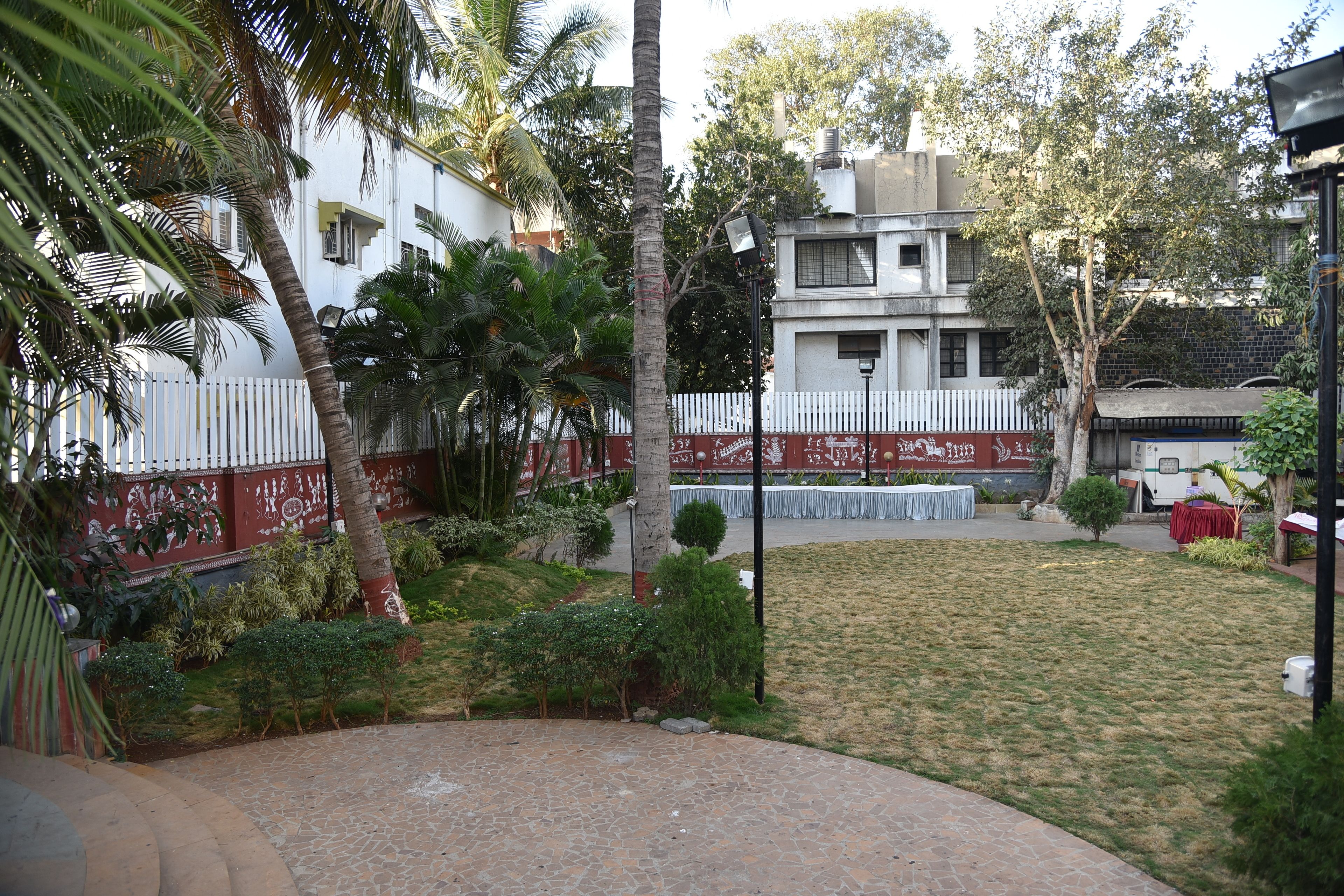 A courtyard with a white fence, palm trees, and a small lawn.