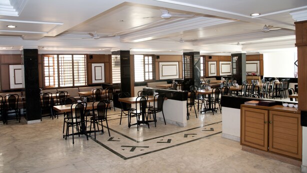 A spacious dining area with multiple tables and chairs, a central bar, and a modern ceiling design.