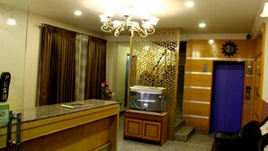 A hotel room with a reception desk, a fish tank, a blue elevator, and a wooden partition with a geometric pattern.