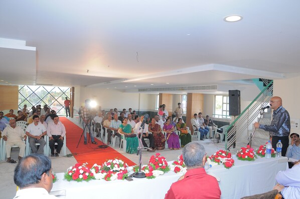 Un salón de conferencias con escenario, público sentado y arreglos florales.