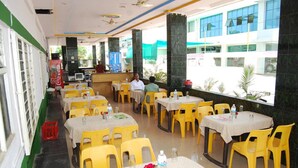 A restaurant with yellow chairs and tables, a Coca-Cola cooler, and a view of buildings outside. - Hotel Utsav (Rahata)
