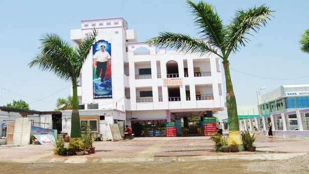A hotel with a large billboard, multiple floors, and a paved entrance area with palm trees. - Hotel Utsav (Rahata)