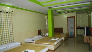 A room with three beds, a green accent wall, and a ceiling fan. - Hotel Utsav (Rahata)