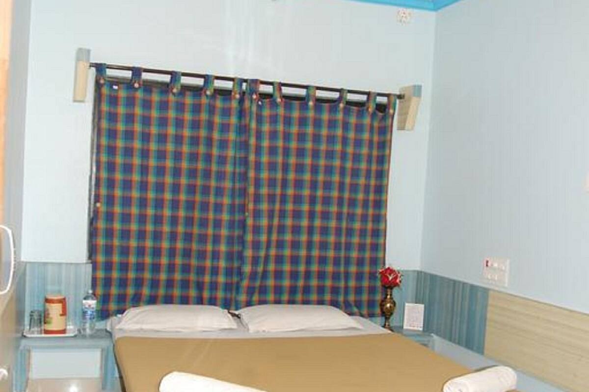 Une chambre à coucher avec un lit, un ventilateur de plafond, une fenêtre avec des rideaux à carreaux et une table de chevet avec une lampe.