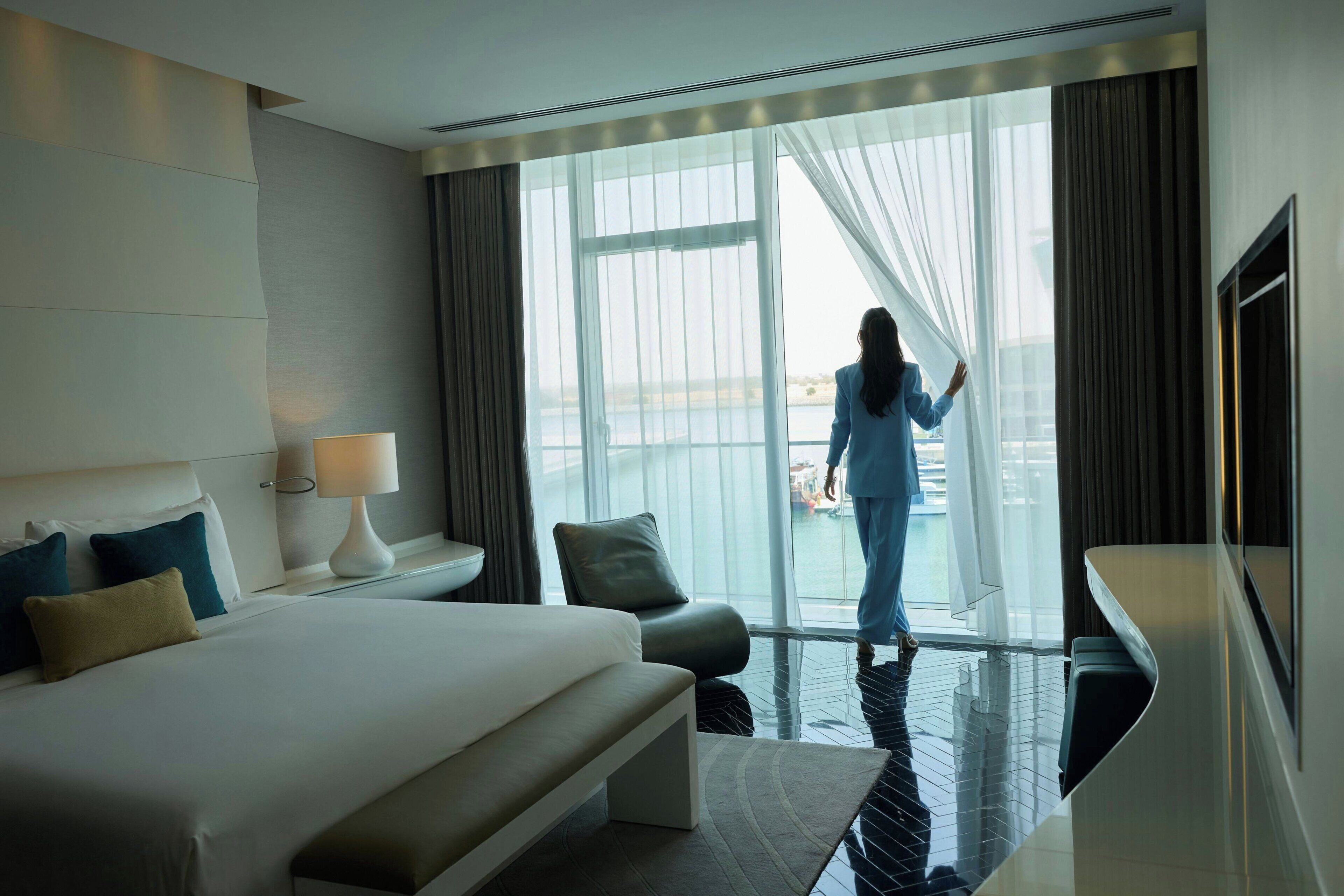 Une chambre d’hôtel moderne dotée d’un grand lit, d’un coin salon, d’une télévision et offrant une vue sur la mer grâce à une grande fenêtre.