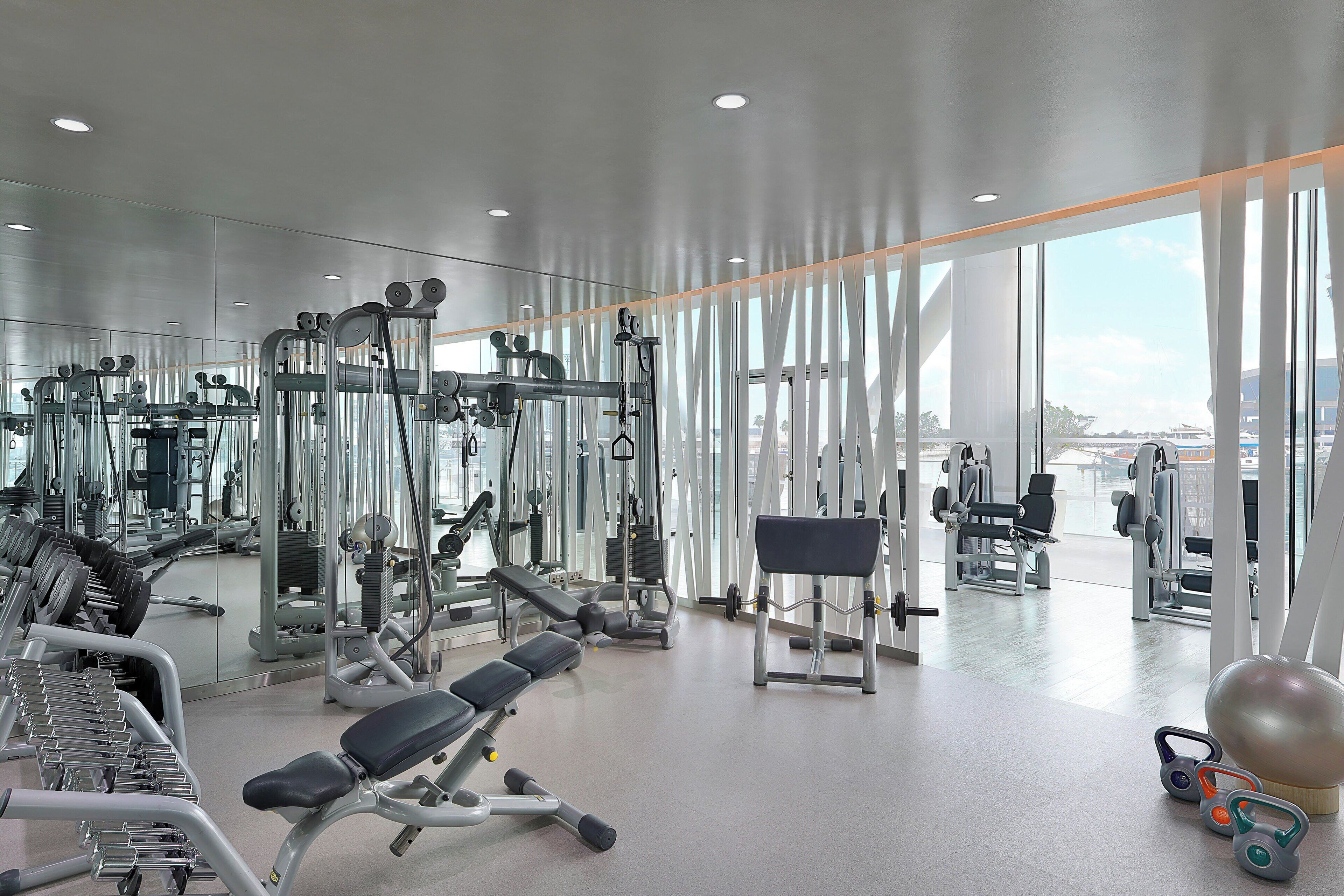 Un gimnasio moderno con diversos equipos de ejercicio, ventanas amplias y vistas a la ciudad.
