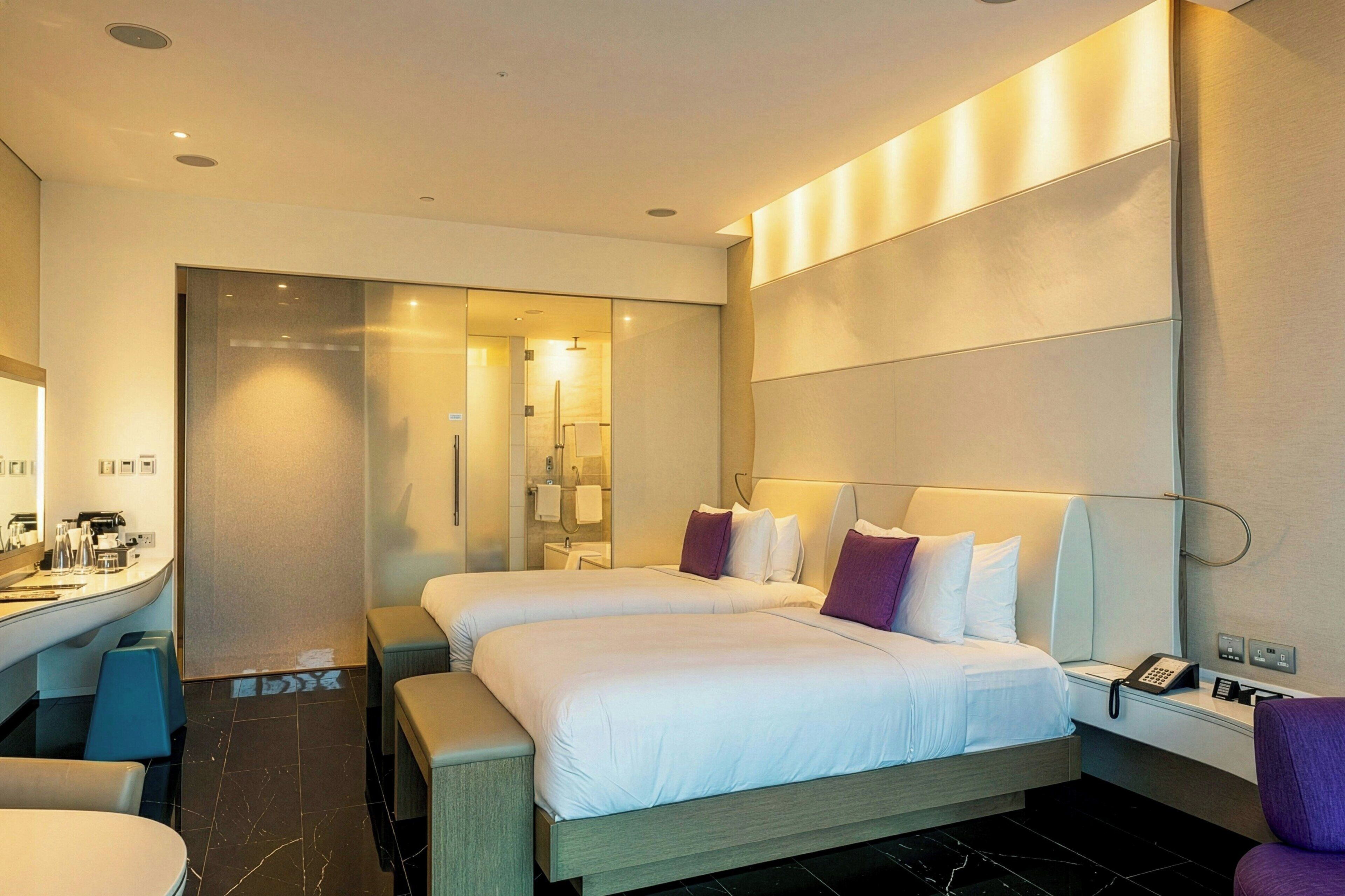 Habitación de hotel con dos camas, un espacio para sentarse, un baño y un mostrador de recepción.