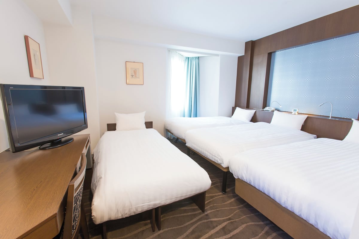 A hotel room with two beds, a TV on a wooden dresser, and a large window with curtains.