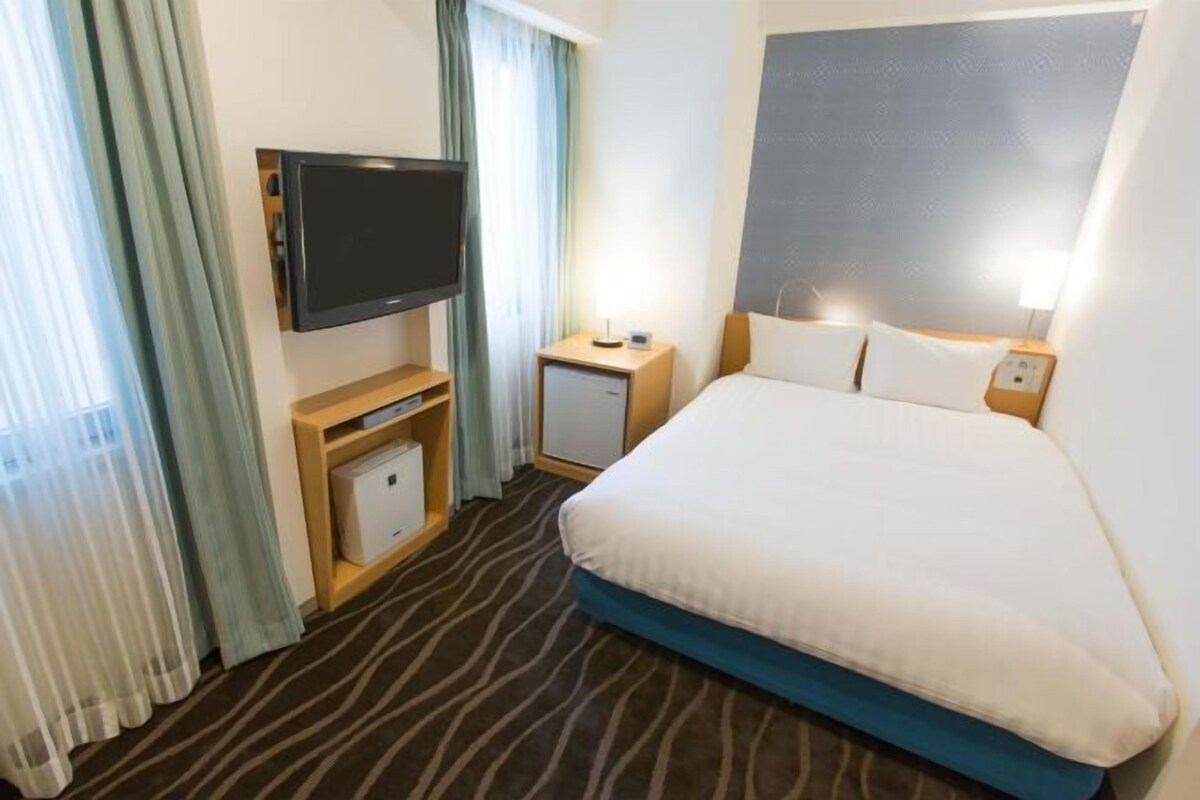 A hotel room with a bed, a television, a bedside table, and a small cabinet.
