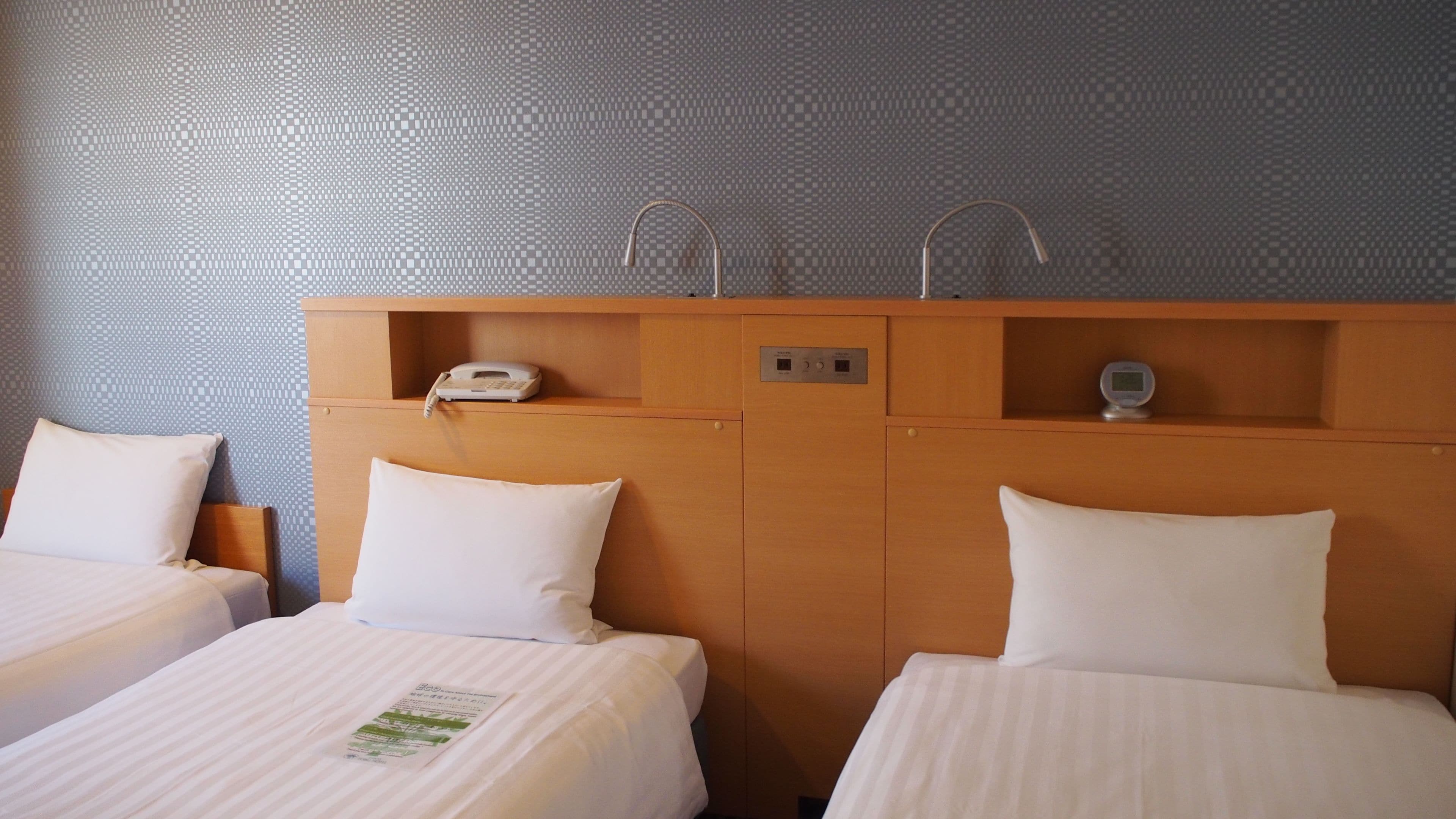 Una habitación de hotel con dos camas, un cabecero de madera, un teléfono y un reloj digital.
