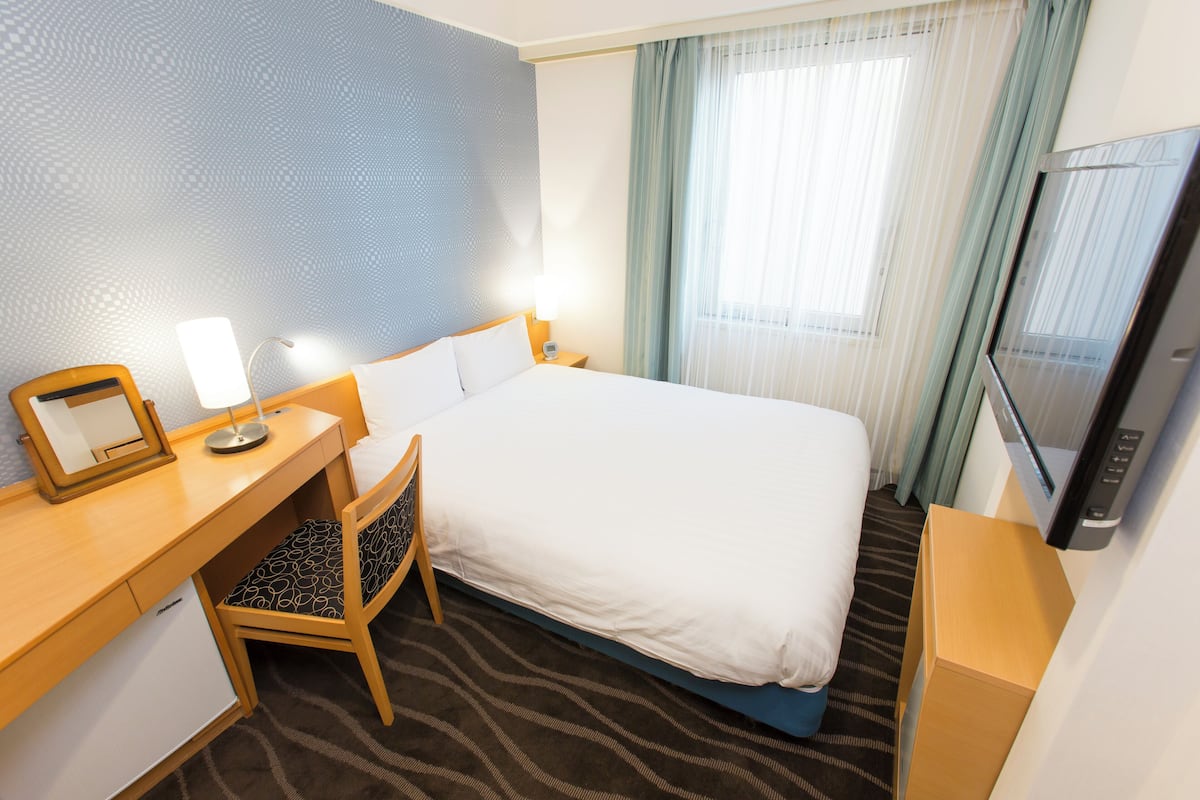 A hotel room with a bed, desk, chair, TV, and a small refrigerator.