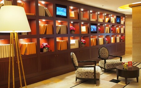 A lobby with a wall of bookshelves, two patterned chairs, a floor lamp, and a small round table.