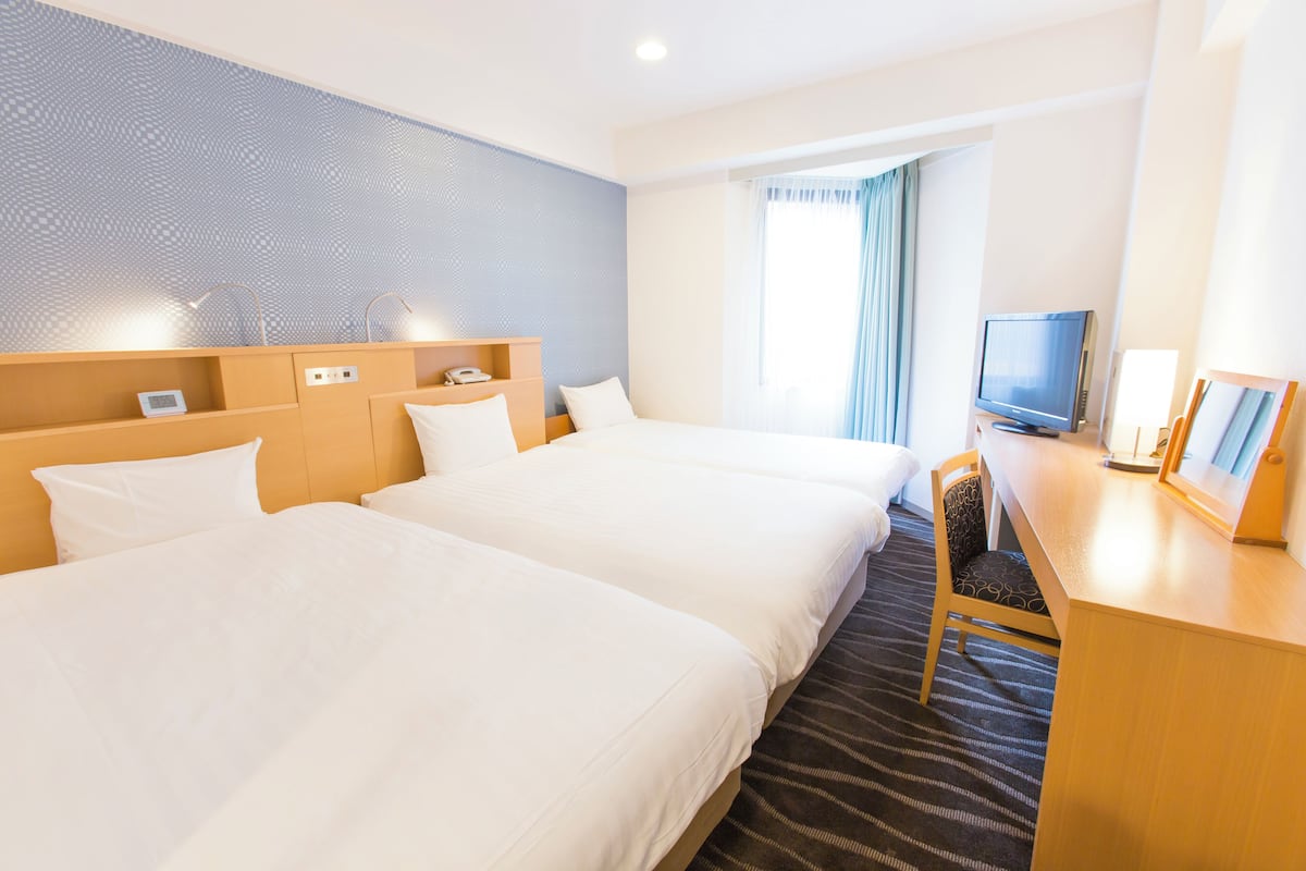 A hotel room with two beds, a desk with a TV, and a window with curtains.