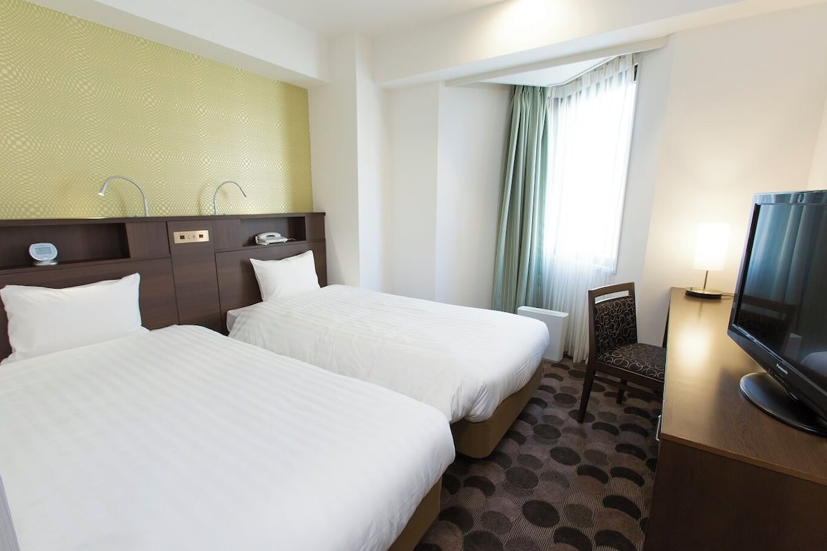 A hotel room with two beds, a television, a desk, and a window with curtains.