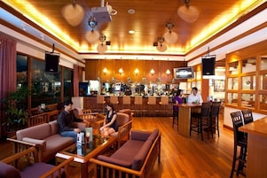 Zona de bar con suelo de madera, asientos acolchados y una barra.