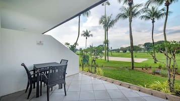 Een terras met een tafel en stoelen, met uitzicht op een golfbaan met palmbomen en een heldere lucht.