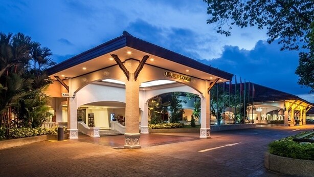 A hotel entrance with a covered walkway, palm trees, and a well-lit facade. - Orchid Country Club (Singapore)