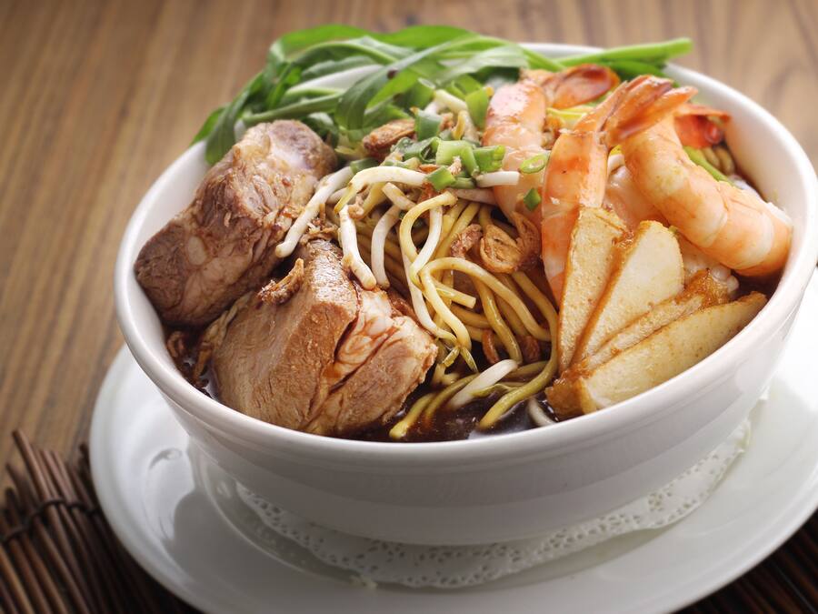 Un tazón de sopa de fideos con diversos ingredientes, como camarones, carne y verduras.