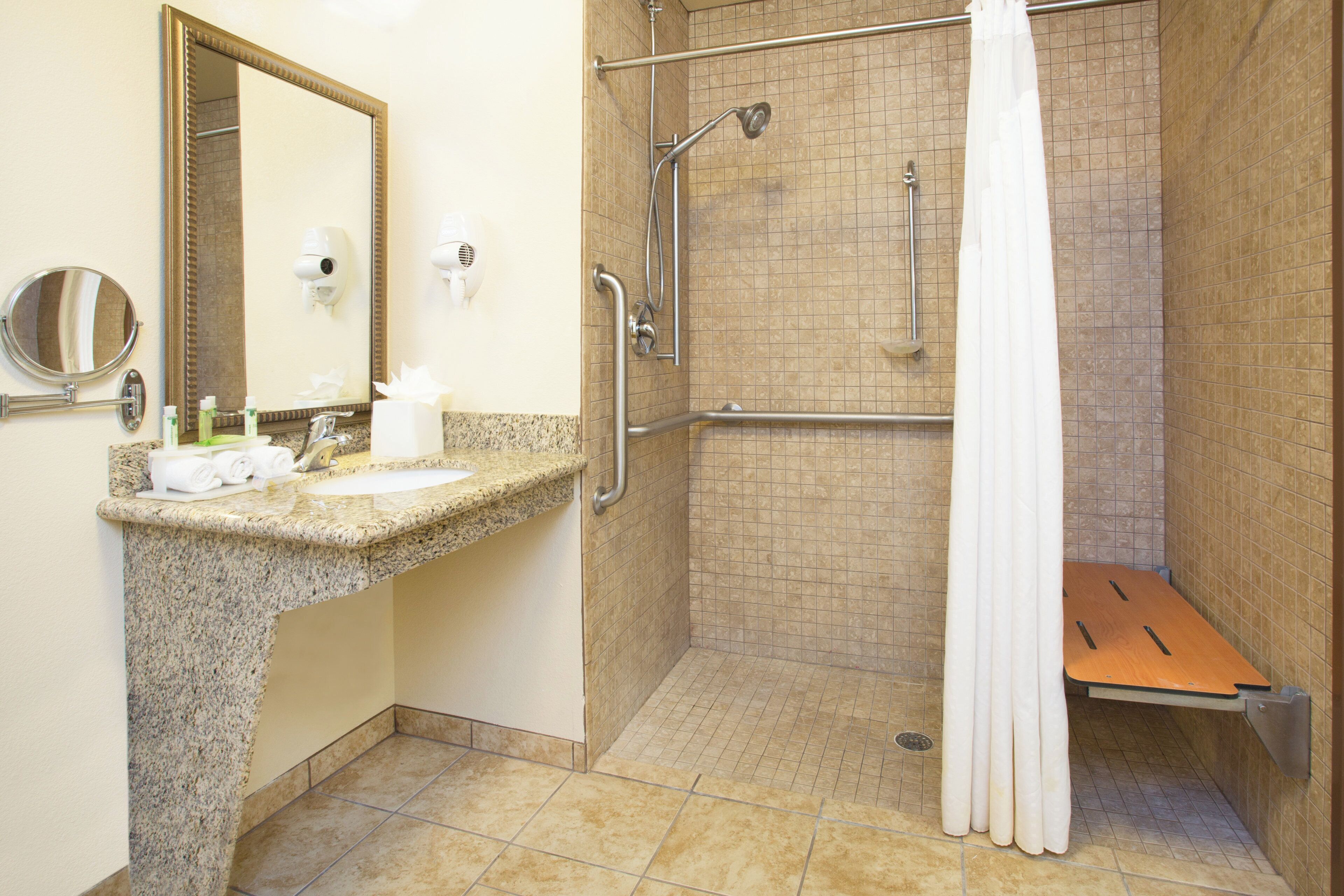 Baño con encimera de granito, lavabo, espejo, cabezal de ducha manual, cortina de ducha y barra de apoyo.