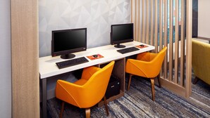 Un espace de bureau moderne comprenant deux bureaux, chacun équipé d’un écran d’ordinateur, d’un clavier et d’une souris. On y trouve également deux chaises orange vif et un canapé jaune.