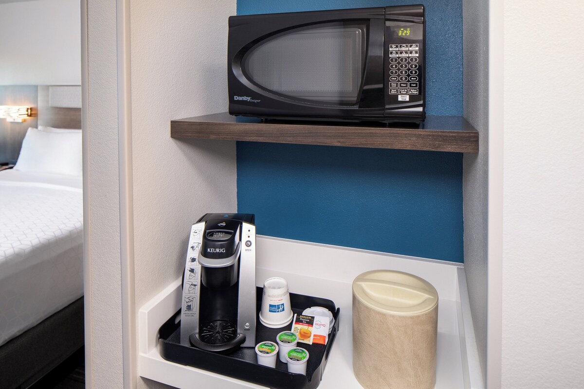 Une chambre d’hôtel équipée d’un four à micro-ondes posé sur une étagère, d’une machine à café et d’un plateau avec des tasses et des condiments.