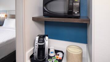 A hotel room with a microwave on a shelf, a Keurig coffee maker, and a coffee pod.