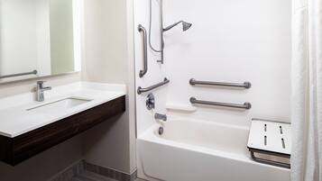 Un baño con lavamanos blanco, bañera con barras de apoyo y ducha.