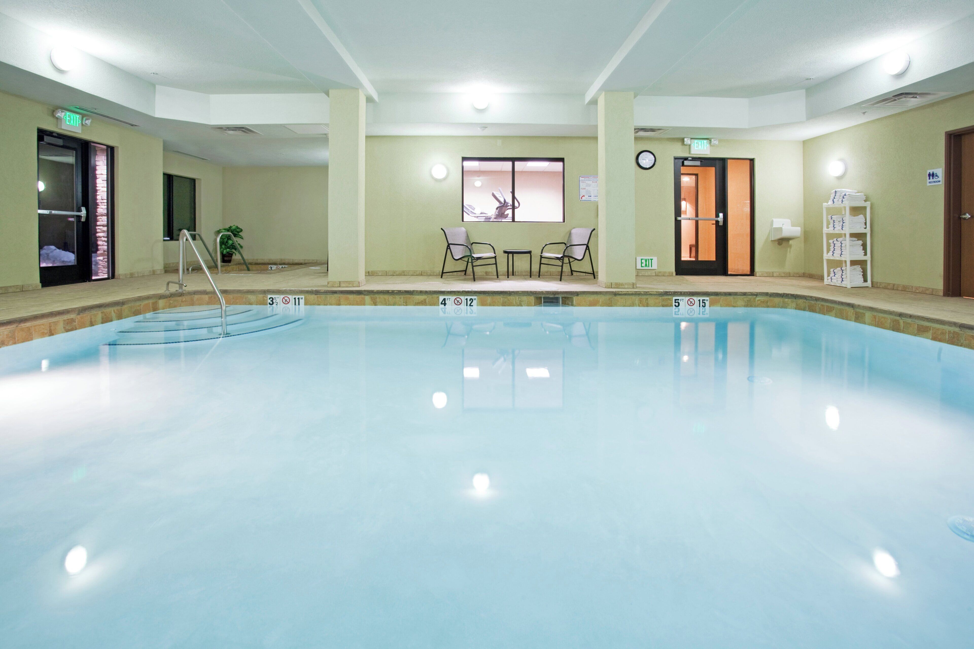 Una amplia piscina cubierta con indicaciones claras de profundidad, un área de descanso con sillones y una recepción.