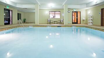Una amplia piscina cubierta con indicaciones claras de profundidad, un área de descanso con sillones y una recepción.