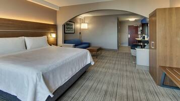 A hotel room with a large bed, a desk, a chair, a sofa, and a kitchenette area.