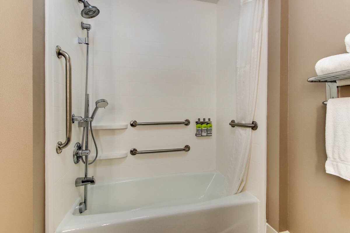Une salle de bain équipée d’une baignoire, de barres d’appui, d’un pommeau de douche et d’un porte-serviettes.