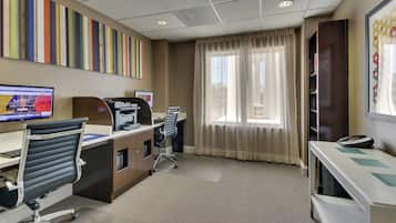 A hotel room with a desk, chair, computer, telephone, and a window with curtains.