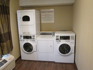 A laundry area with stacked washers and dryers, a sign indicating it's for guest use, and a vent on the left.
