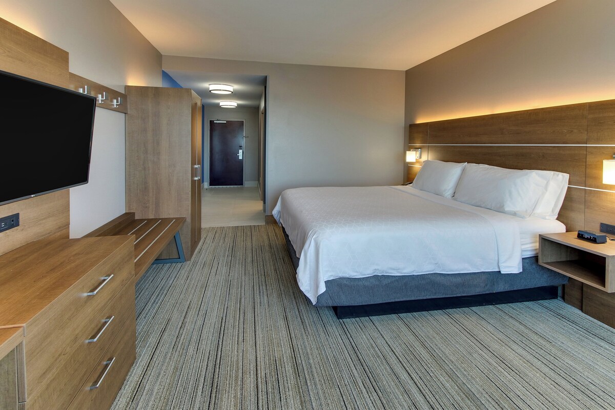 Habitación de hotel con cama, mesita de noche, televisor, armario de madera y piso alfombrado.