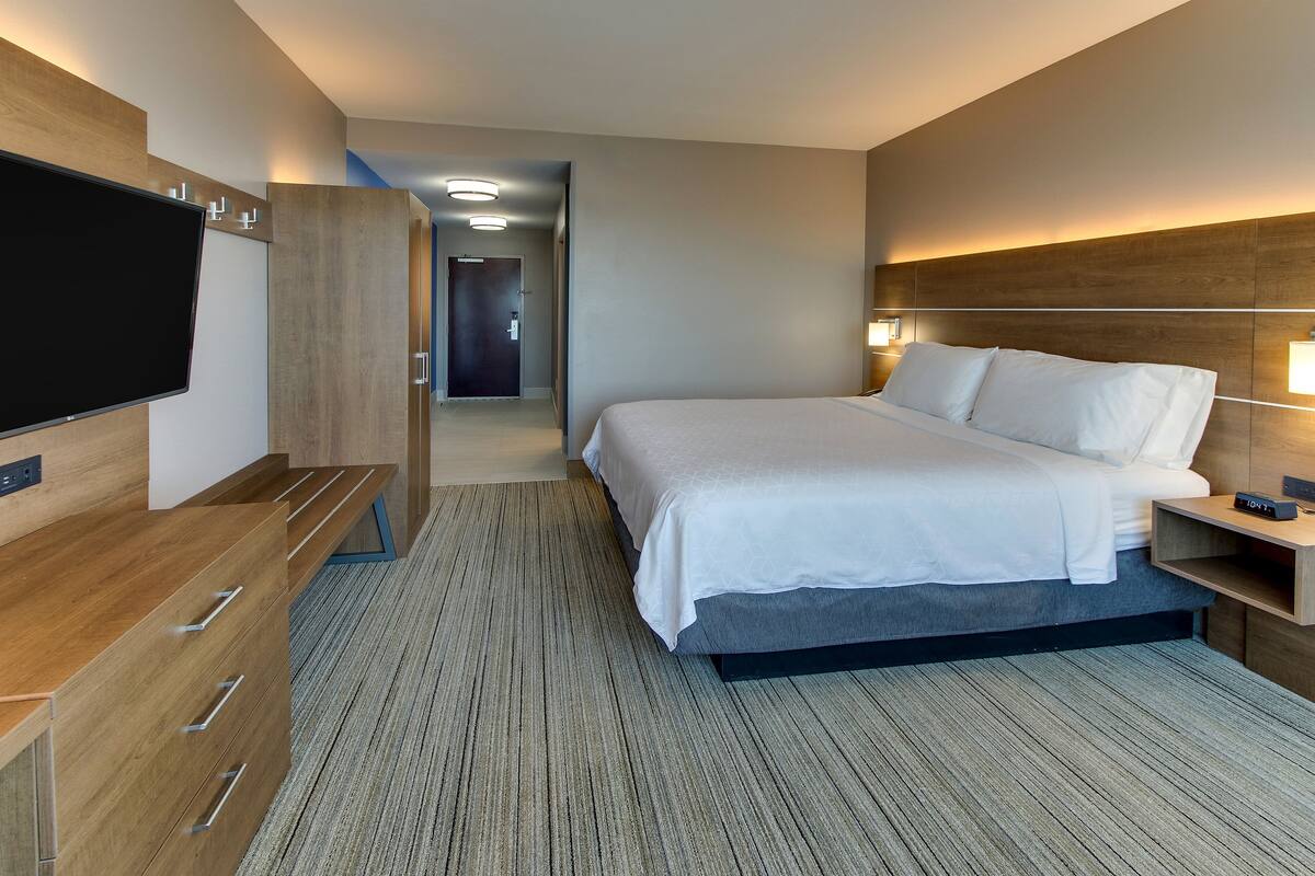 Une chambre d’hôtel moderne équipée d’un lit, d’une télévision, d’un bureau et d’un dressing.