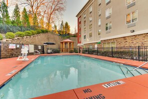 Una piscina con un letrero que prohíbe los clavados, un pabellón y un muro de piedra con árboles al fondo.