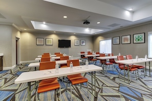 Une salle de conférence équipée de tables, de chaises, d’un projecteur et ornée d’œuvres d’art encadrées aux murs.