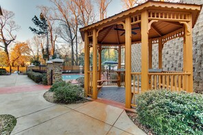 Una pérgola con un muro de piedra de fondo, un camino empedrado y una zona de piscina.