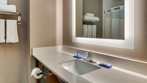 Et badeværelse med vask, spejl, håndklædestang og toiletpapirholder.