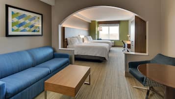 A hotel room with a blue sofa, a wooden coffee table, a bed with white bedding, and a large mirror reflecting the room.