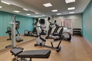 Een fitnessruimte met cardioapparatuur, een bankje en een spiegel aan de muur.
