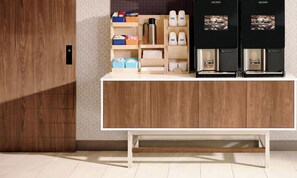 Una cocina moderna con armarios de madera, encimera blanca y dos máquinas de café.