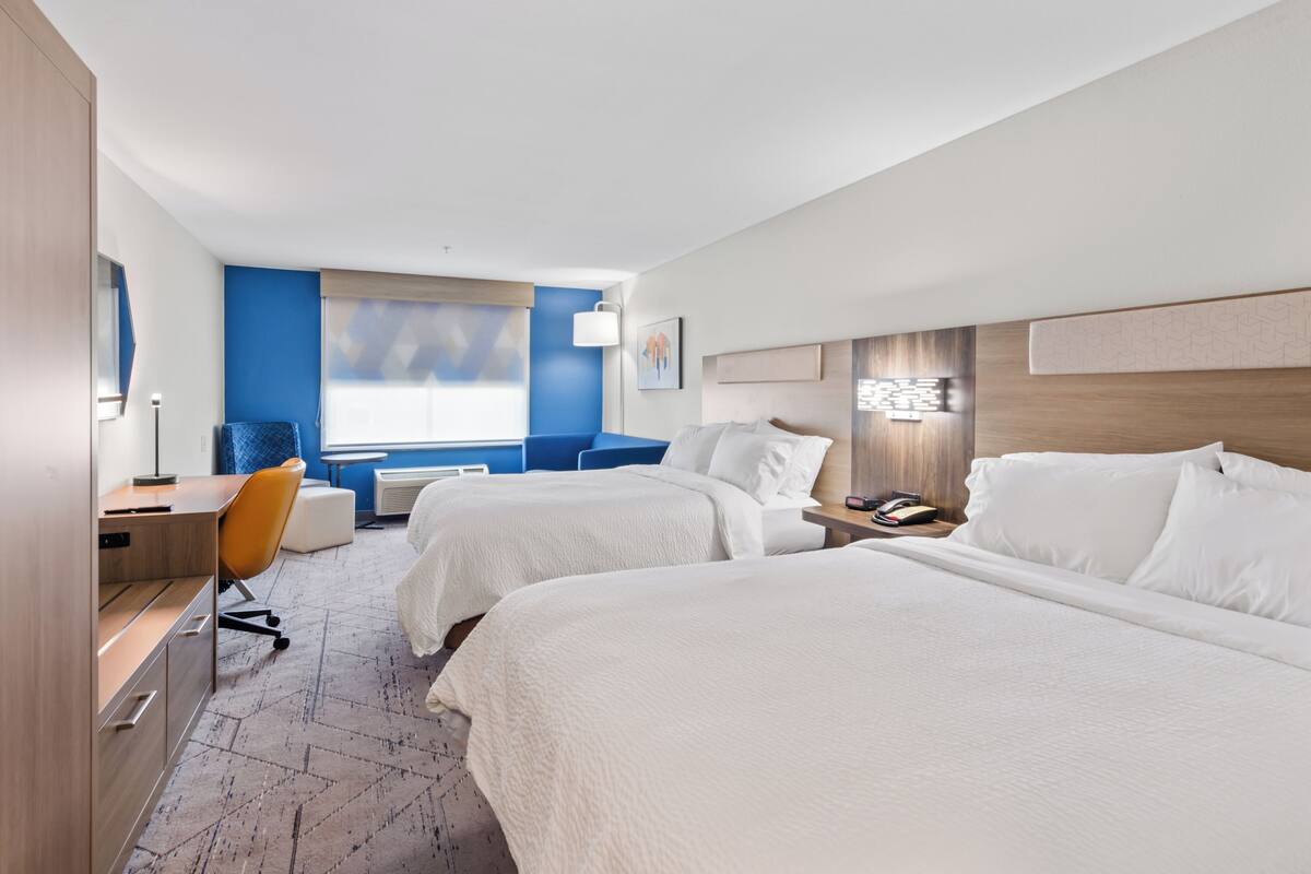 A hotel room with two beds, a desk, a chair, and a window with a view.