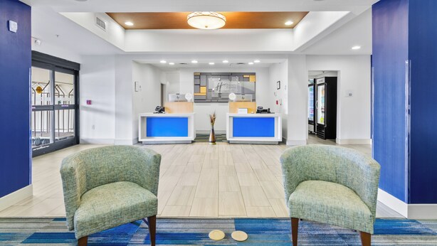 A reception area with two reception desks, a blue carpet, and two green armchairs. - Holiday Inn Express Hotel & Suites Mount Airy by IHG (Mount Airy)