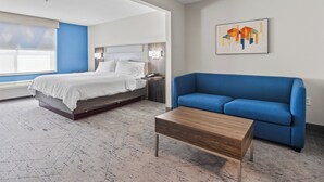 A modern hotel room with a bed, a blue sofa, and a wooden coffee table. - Holiday Inn Express Hotel & Suites Mount Airy by IHG (Mount Airy)