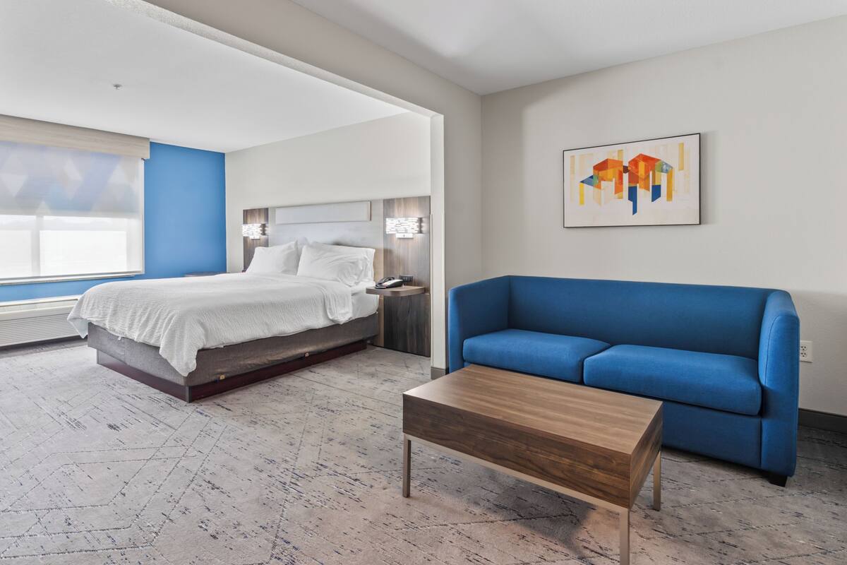 A modern hotel room with a bed, a blue sofa, and a wooden coffee table.