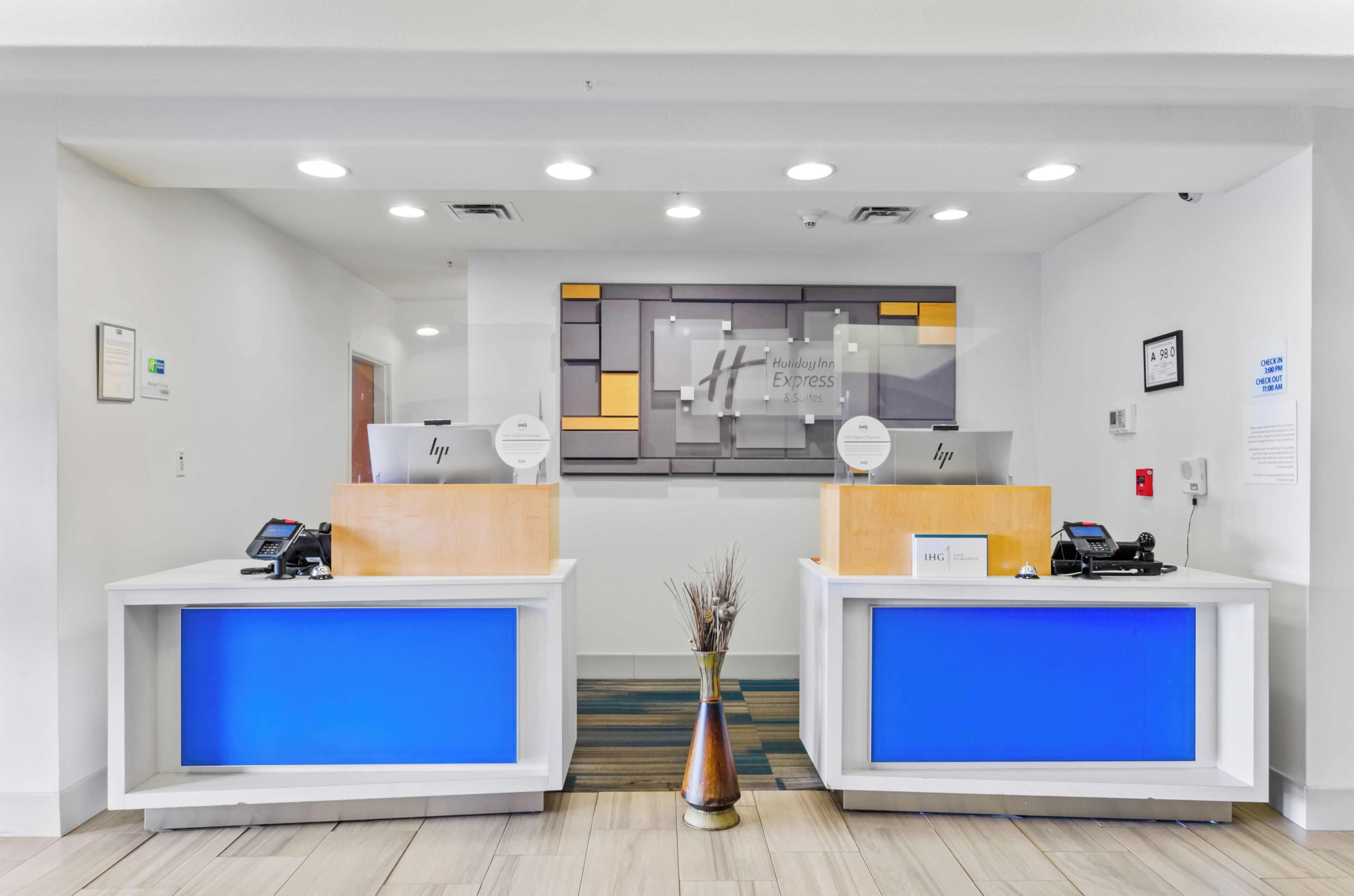 Een hotel receptie met twee balies, een centraal informatiebord en een vaas met decoratieve takken.