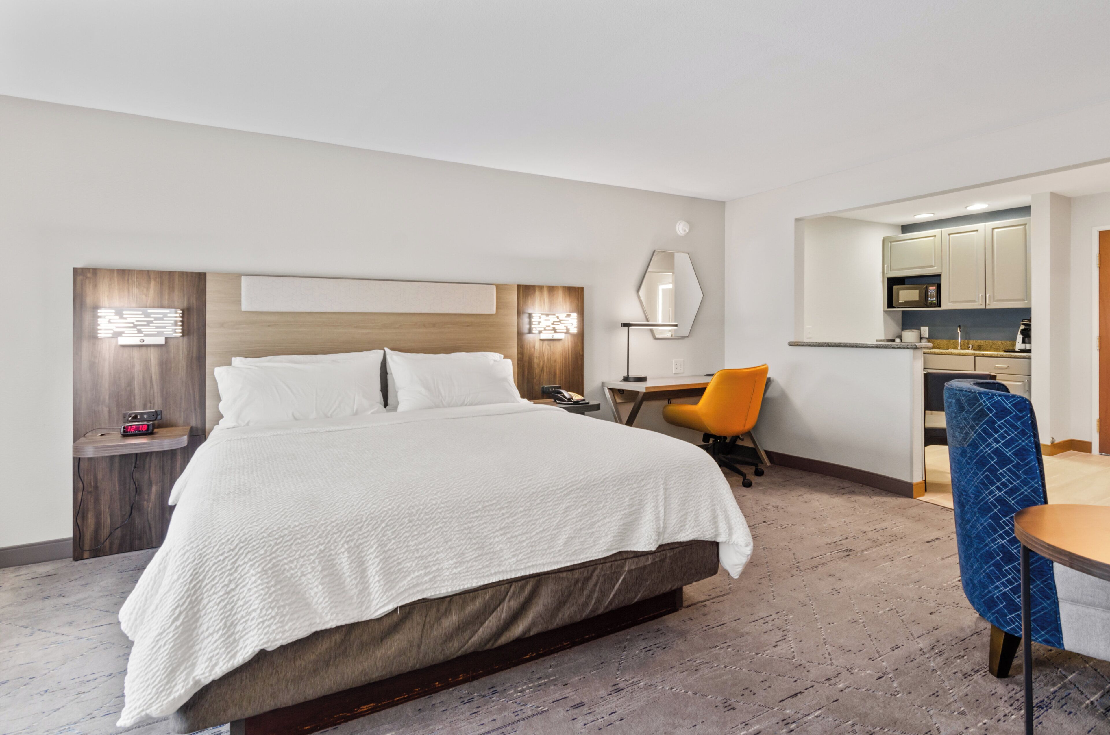 Et hotelværelse med en stor seng, et skrivebord med stol, et lille tekøkken og et spejl.