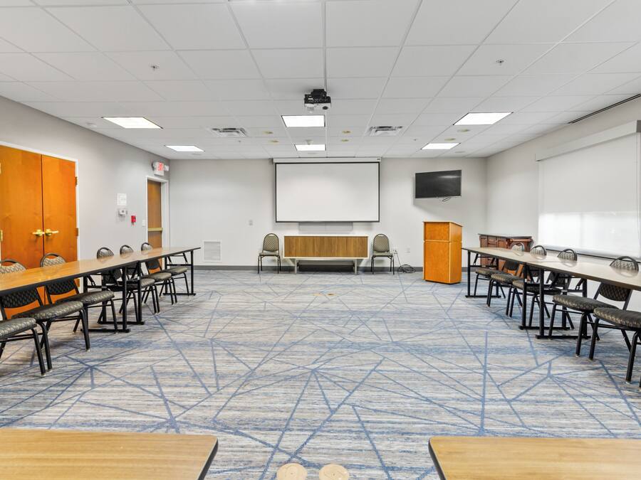 A conference room with a long table, chairs, a projector, and a screen.
